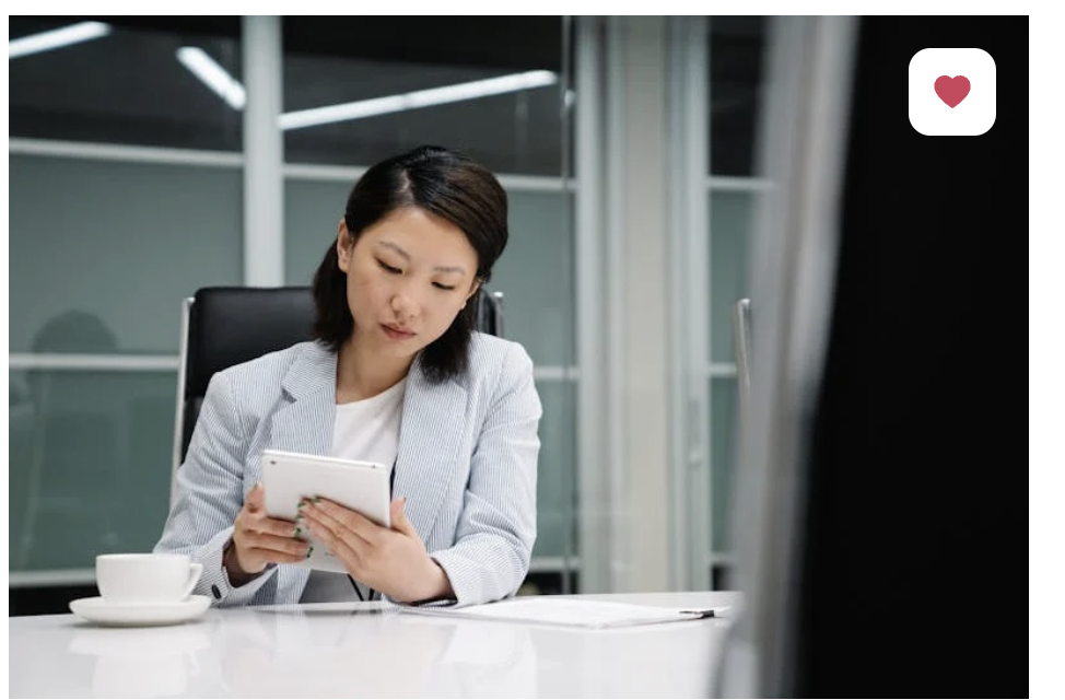 A professional woman looks at an iPhone while sitting at a computer in an office. When marketing your business, it's vital to ask: what story is your customer telling themselves?